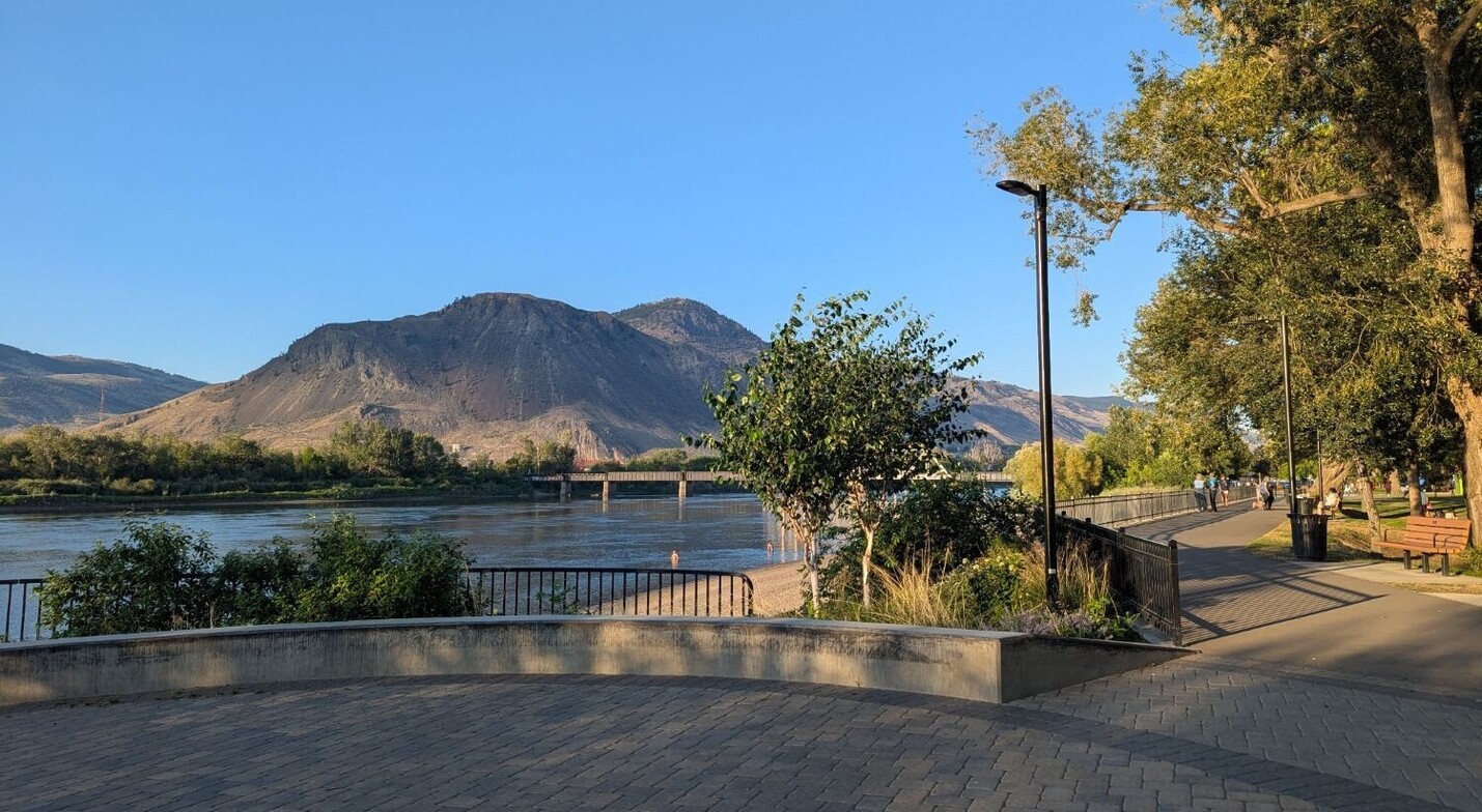 Riverside Park in Kamloops, with a paved path beside the Thompson River and a mountain in the background.